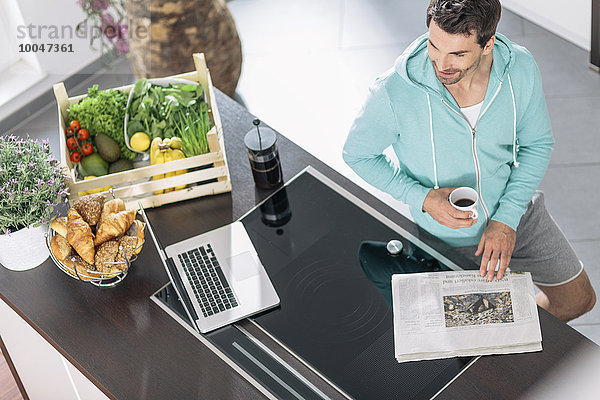 Mann mit Tasse Kaffee  Laptop und Zeitung in der Küche