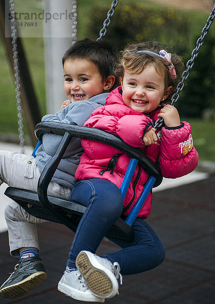 Spanien  Kleines Mädchen und Junge lachend auf der Schaukel sitzend