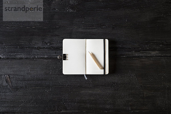 Geöffnetes Notizbuch und Bleistift auf schwarzem Holz