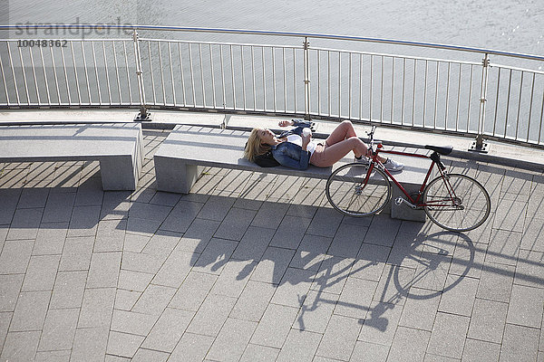 Deutschland  Düsseldorf  blonde Frau liegt auf einer Bank und ruht sich vor dem Rhein aus.