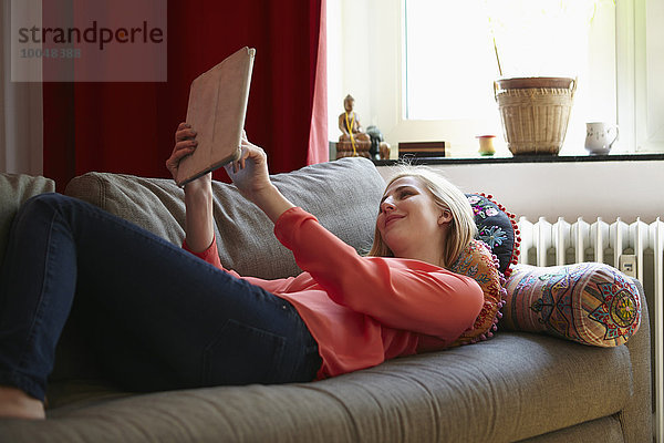 Lächelnde junge Frau entspannt mit digitalem Tablett auf der Couch zu Hause