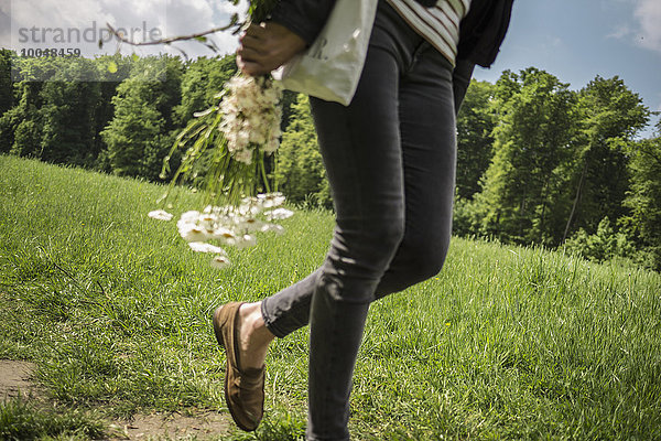 Frau geht mit Blumen auf der Wiese spazieren