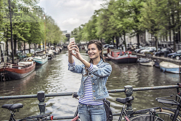 Niederlande  Amsterdam  Touristin mit Smartphone vor dem Stadtkanal