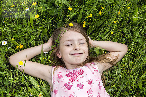 Porträt eines lächelnden Mädchens mit geschlossenen Augen auf einer Blumenwiese liegend
