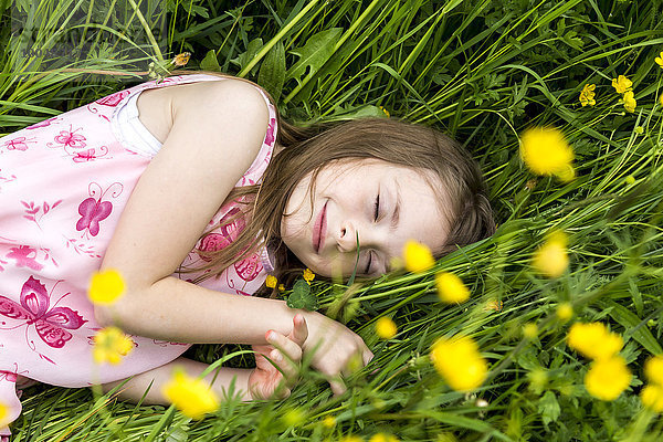 Lächelndes kleines Mädchen mit geschlossenen Augen auf einer Blumenwiese liegend