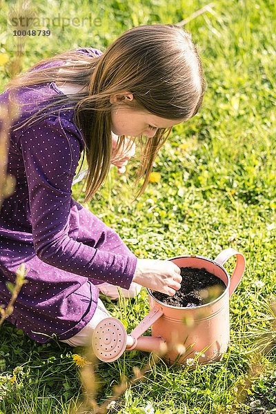 Kleines Mädchen kniend auf der Wiese mit Gießkanne gefüllt mit Erde