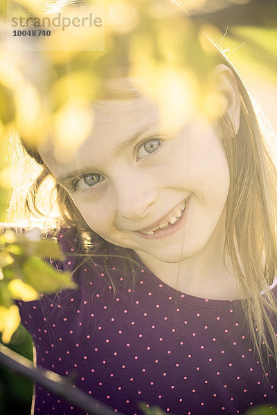 Porträt eines lächelnden kleinen Mädchens  das durch Zweige eines Baumes schaut.