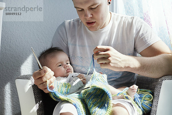 Junger Vater strickt mit Baby auf dem Schoß