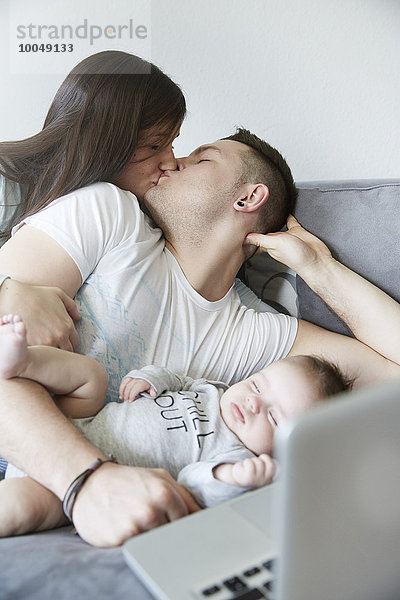 Junger Mann und Frau beim Küssen mit Baby auf der Couch liegend
