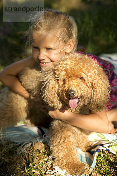 Fröhliches Mädchen umarmt Hund auf Decke