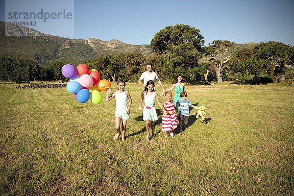 Glückliche Familie läuft mit Luftballons auf der Wiese