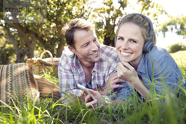 Glückliches Paar auf der Wiese mit einer Frau  die Musik vom Smartphone hört.
