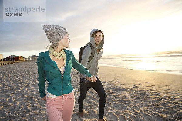 Junges Paar bei Sonnenaufgang am Strand spazieren gehen