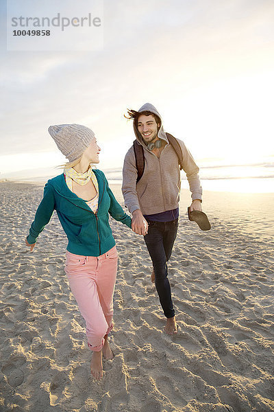 Junges Paar bei Sonnenaufgang am Strand spazieren gehen
