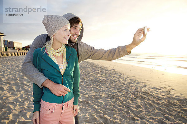 Junges Paar bei Sonnenaufgang mit einem Selfie am Strand