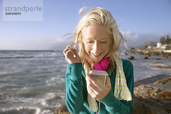 Lächelnde junge Frau mit Handy an der Küste