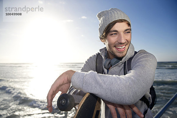 Lächelnder junger Mann mit Longboard an der Küste