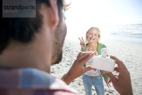 Mann fotografiert glückliche Frau am Strand