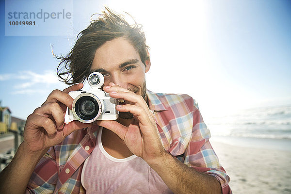 Junger Mann beim Fotografieren am Strand