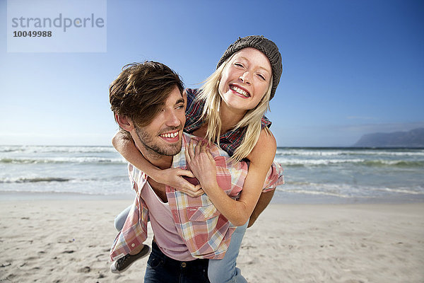 Junger Mann mit Freundin Huckepack am Strand