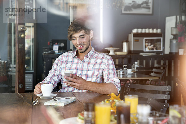 Lächelnder junger Mann in einem Café mit Blick aufs Handy