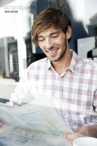 Lächelnder junger Mann in einem Café beim Zeitungslesen