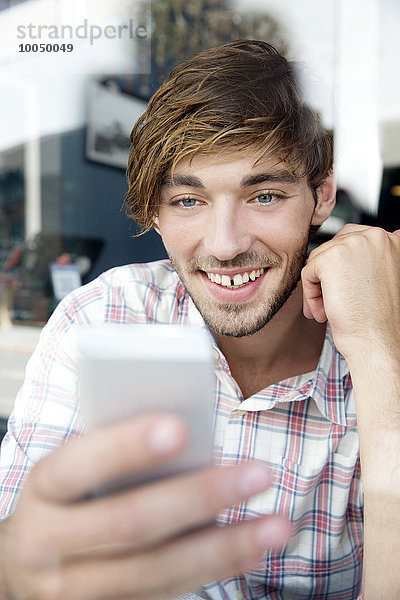 Lächelnder junger Mann in einem Café mit Blick aufs Handy