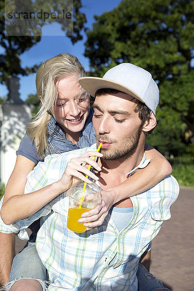 Junger Mann trinkt Erfrischungsgetränk mit Freundin Huckepack