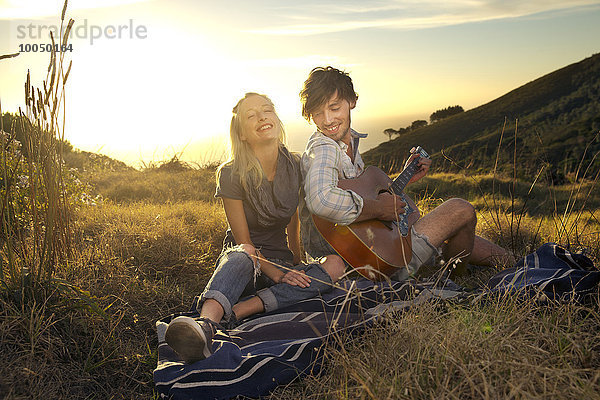 Glückliches junges Paar mit Gitarre auf Decke in der Wiese