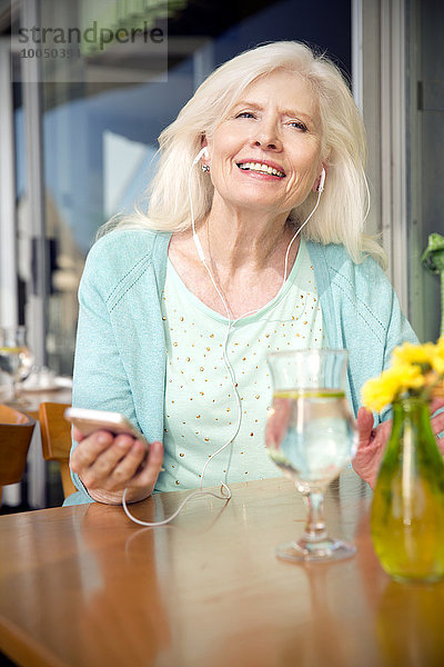 Porträt einer älteren Frau mit Smartphone  die Musik mit Kopfhörern hört.