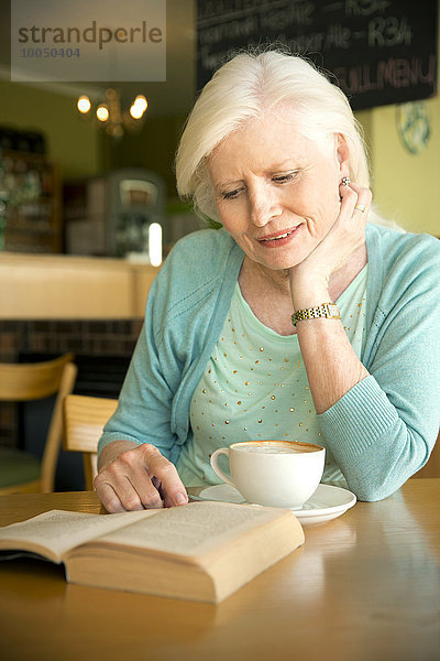 Porträt einer älteren Frau beim Lesen im Café