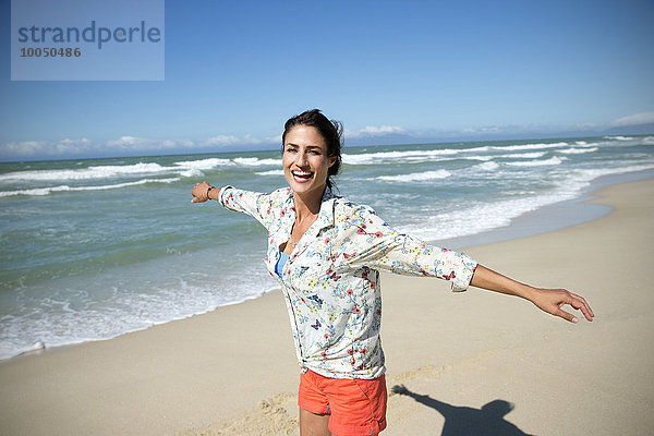 Südafrika  lachende Frau mit ausgestreckten Armen am Strand stehend