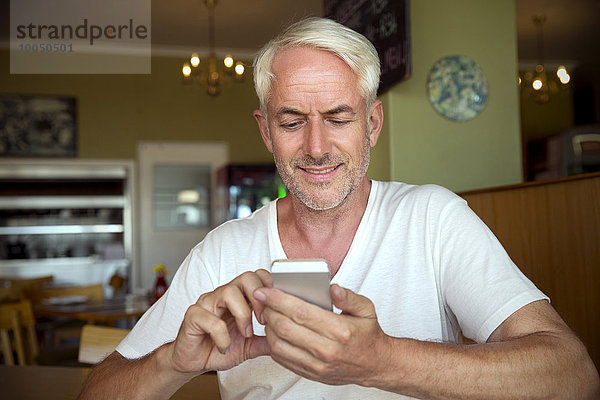 Porträt eines lächelnden Mannes  der mit dem Smartphone im Café sitzt.