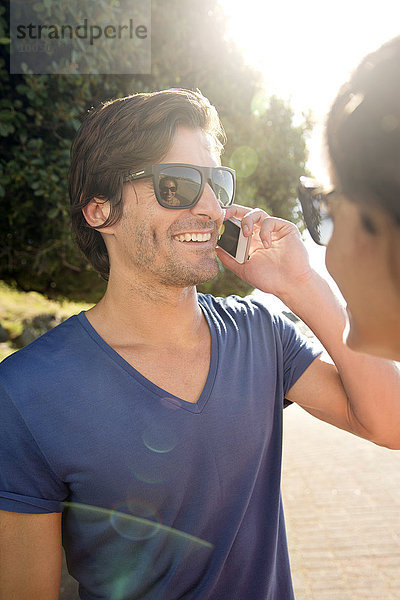 Südafrika  Porträt eines lächelnden Mannes mit Sonnenbrille beim Telefonieren mit Smartphone