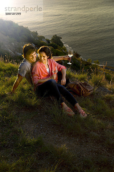 Südafrika  glückliches Paar mit Weißweingläsern an der Küste in der Abenddämmerung