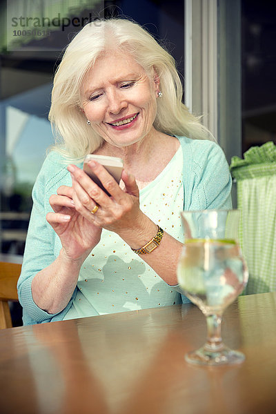 Porträt einer glücklichen Seniorin  die mit dem Smartphone in einem Café sitzt.