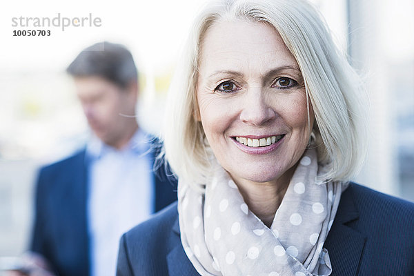 Portrait einer reifen Geschäftsfrau mit Mann im Hintergrund