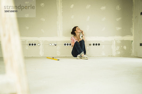 Junge Frau renoviert sitzend an der leeren Wand