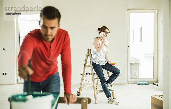 Junge Frau am Telefon mit Mann beim Malen von Holzbrettern im Vordergrund