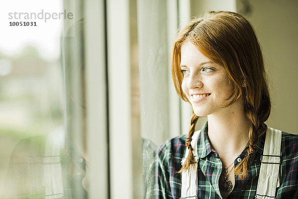 Lächelnde junge Frau schaut aus dem Fenster.