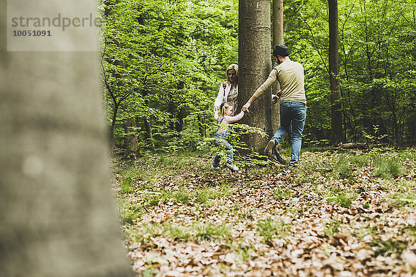 Familie im Wald läuft um den Baumstamm herum