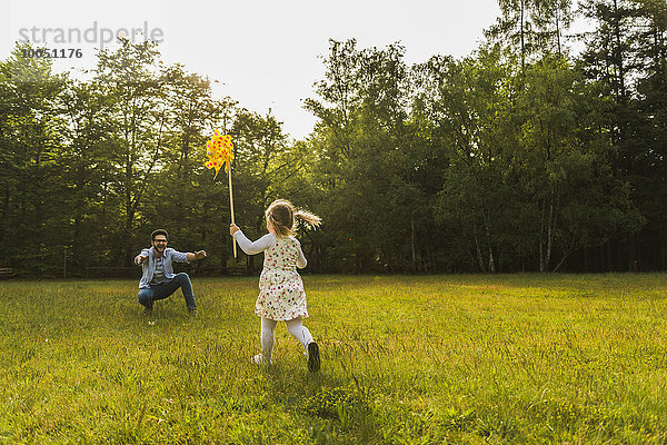 Mädchen mit Papierwindmühle auf der Wiese zum Vater rennend