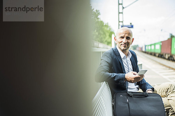 Geschäftsmann mit Handy auf Bahnsteig