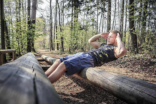 Deutschland  Coburg  Junger Mann beim Sitzen auf einem Fitness-Parcours im Wald