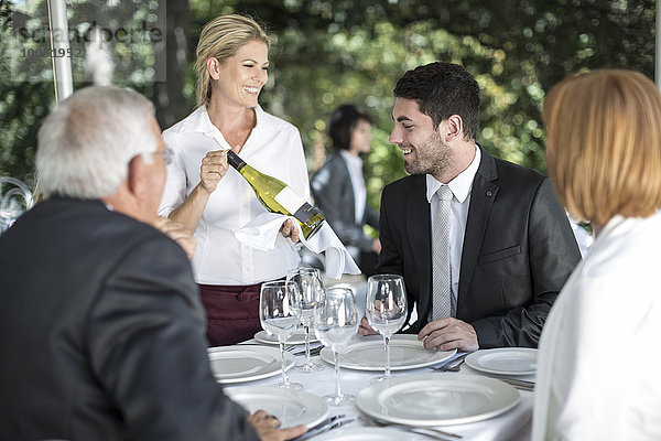 Kellnerin zeigt den Gästen Weißwein am Tisch