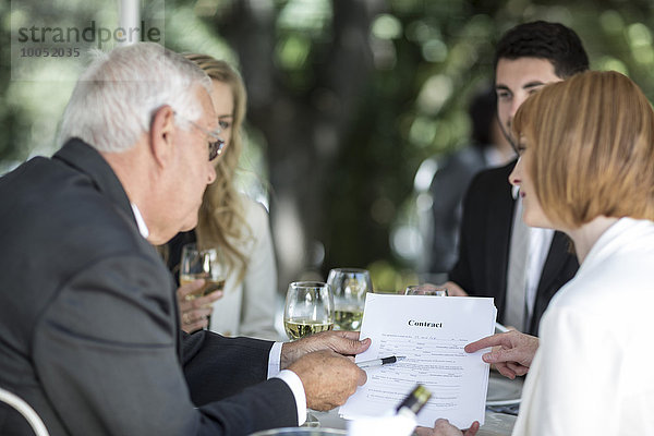 Elegante Leute im Außenrestaurant diskutieren über einen Vertrag