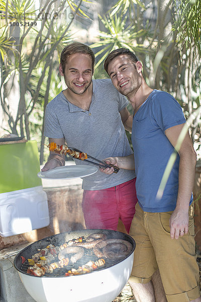 Fröhliches schwules Paar bei der Zubereitung des Essens auf dem Grill