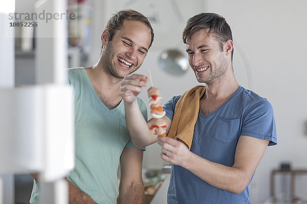 Fröhliches schwules Paar beim Zubereiten von Fleischspieße in der Küche