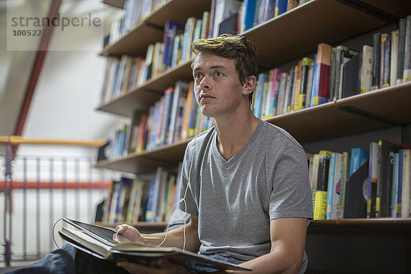 Student mit digitalem Tablett und Kopfhörer in einer Bibliothek