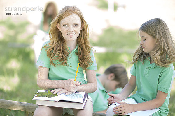 Mädchenporträt mit Schulheft und Blättern im Park